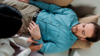 Stockphoto man ligger på ryggen, lukkede øjne, hypnotisør mærker ham på håndleddet. 