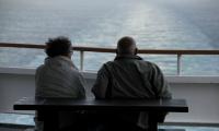Et ældre par sidder på en bænk ved vandet og ser udover havet. 