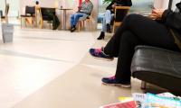 Venteværelse ved hospital eller læge, mennesker sidder og venter med smartphone i hånden. 