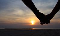 To hænder holder i hånd foran solnedgang ved stranden