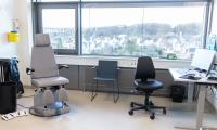 Billede viser et undersøgelsesrum ved den nye dermatologiske afdeling på AAUH, et klassisk lægekontor med kontorplads, stol til patient og en vinduer med flot udsigt over byen i baggrunden. 