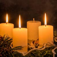 Adventskrans i gran og fire hvide stearinlys hvor tre er tændt, dæmpet stemningsfuld belysning. 