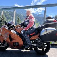 Privatfoto af Liselott Blixt, formand for Psoriasisforeningen, der sidder på sin røde motorcykel foran et bjerglandskab. 
